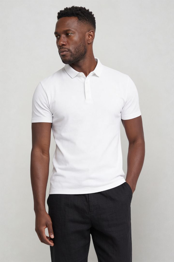 Man wearing a white polo shirt and dark pants against a plain background