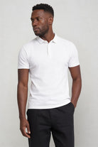 Man wearing a white polo shirt and dark pants against a plain background