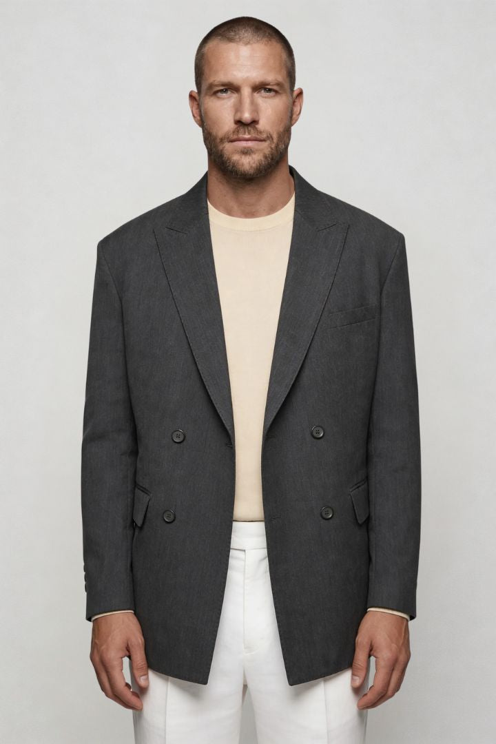 Man wearing a gray blazer over a beige shirt and white pants on a plain background