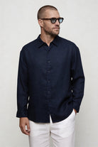 Man wearing a linen navy button-up shirt and white pants against a plain background